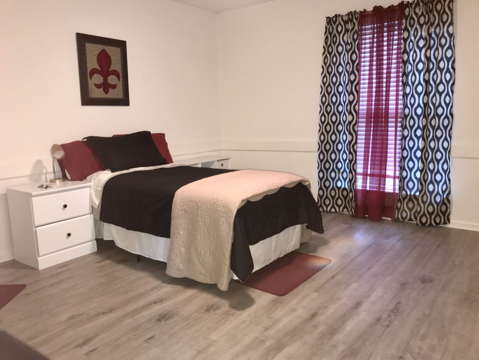 Typical bedroom for exiting incarcerated people housed by Louisiana Parole Project apartment: simple bedroom with a small bed, nightstand and shades covering the windows