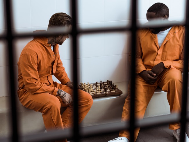 Two incarcerated people play chess behind prison bars