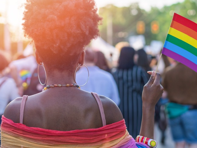 Woman in crowd holding a rainbow flag and wearing a rainbow shawl over her outfit